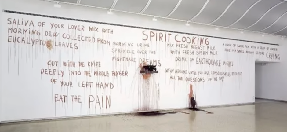 Marina Abramowicz pisząca o „spirit cooking” (dosłownie: gotowanie duchów). Oficjalnie miała to być forma sztuki, ale w praktyce były to np. teksty z książki kucharskiej zapisane na ścianie świńską krwią.